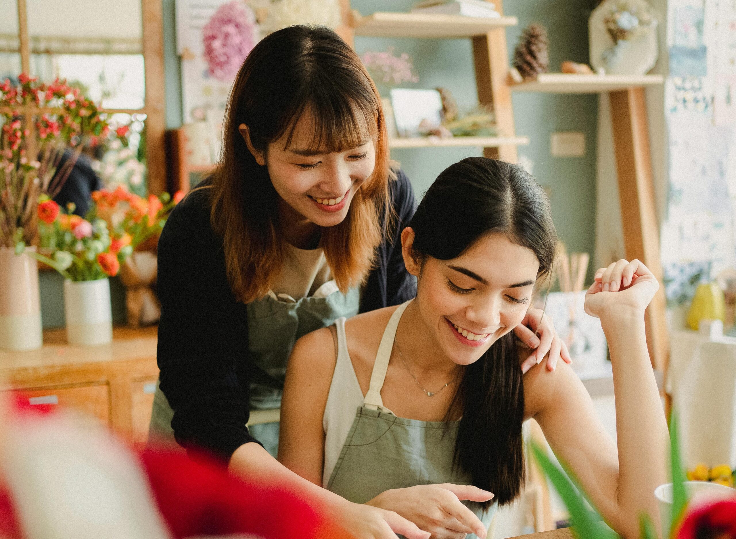 Two women in aprons smiling and working together in a cozy shop.