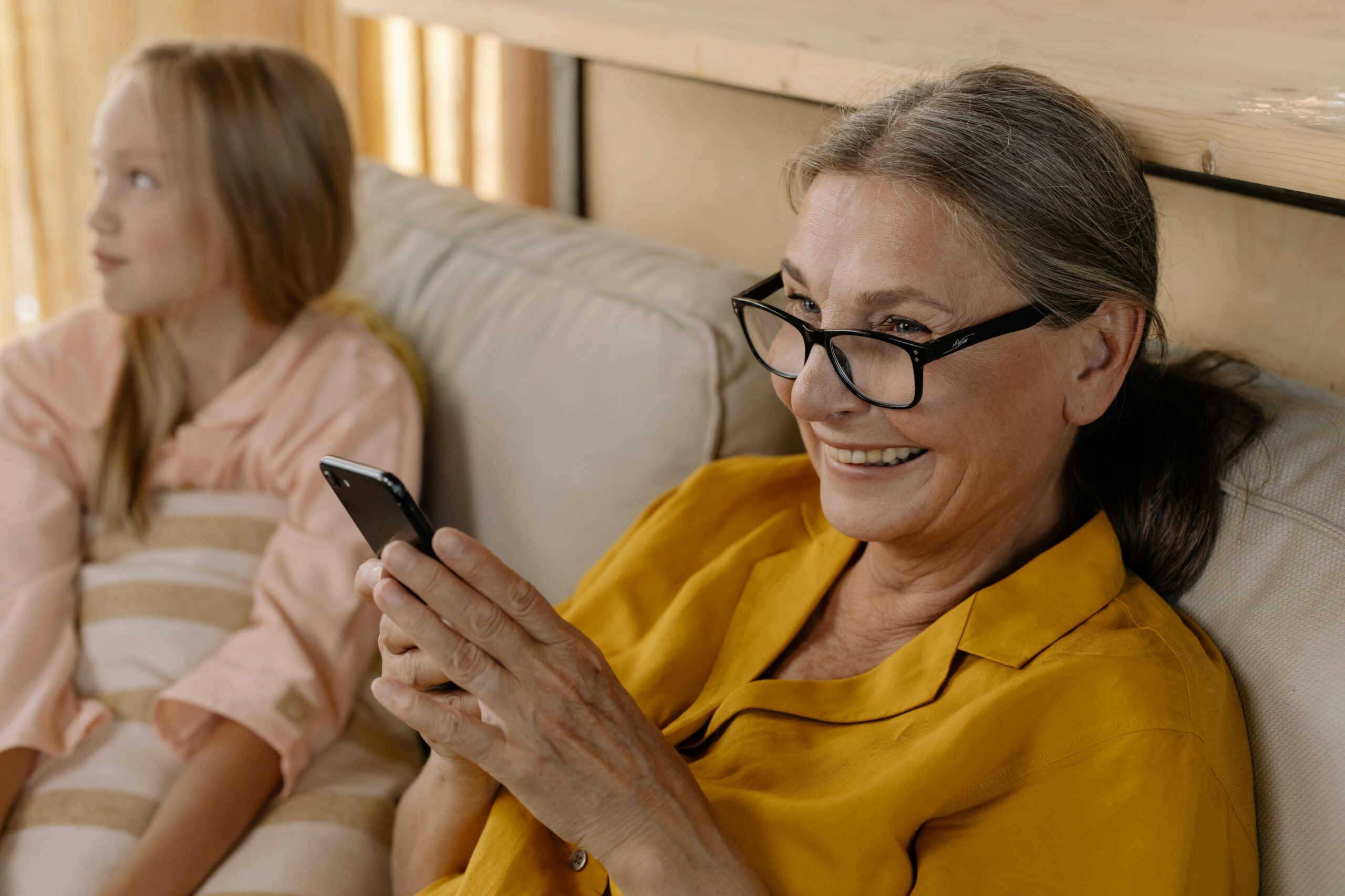 Elderly woman smiling at her phone, young girl sitting beside her.