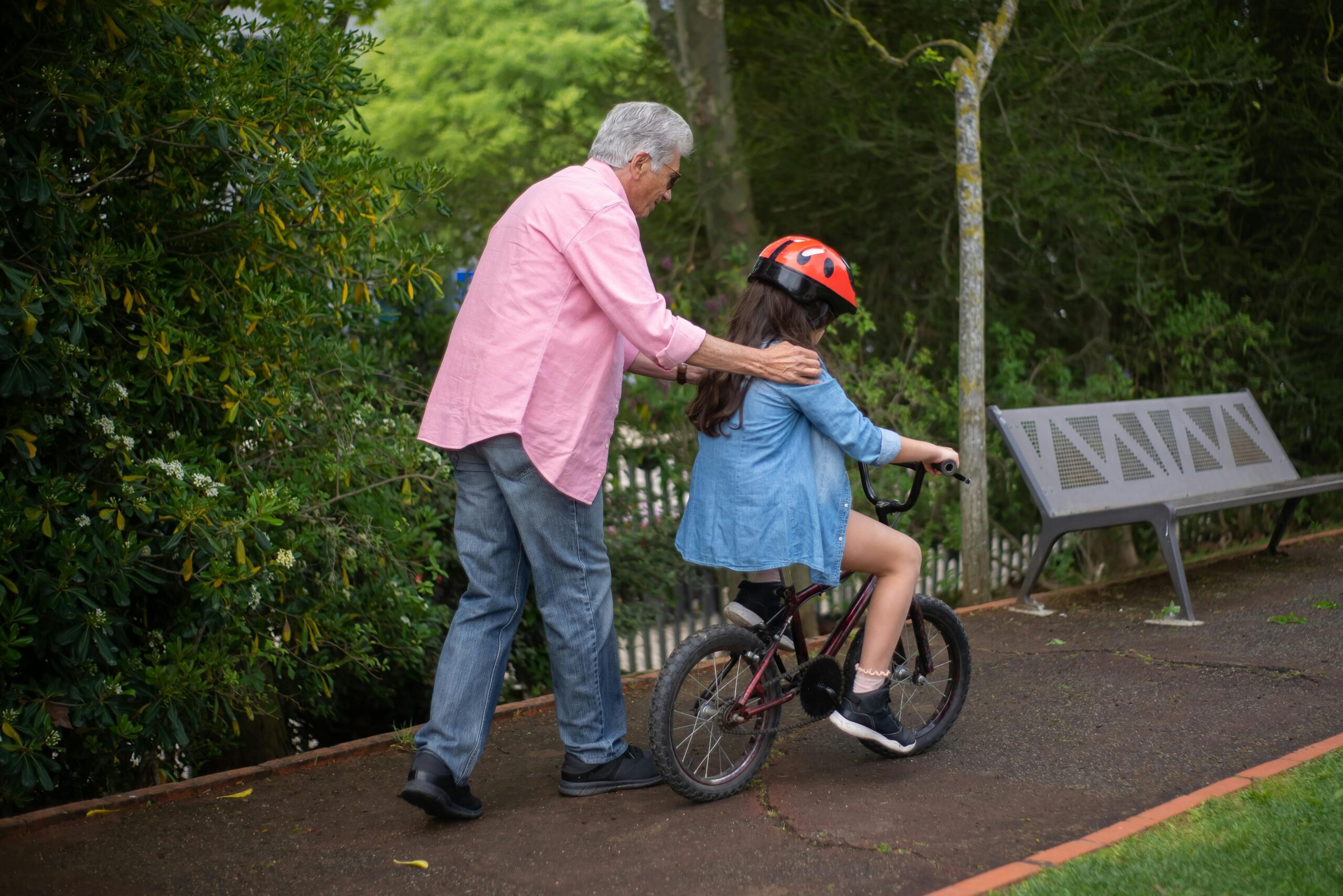Elderly man helping a young girl ride a bicycle in a park.