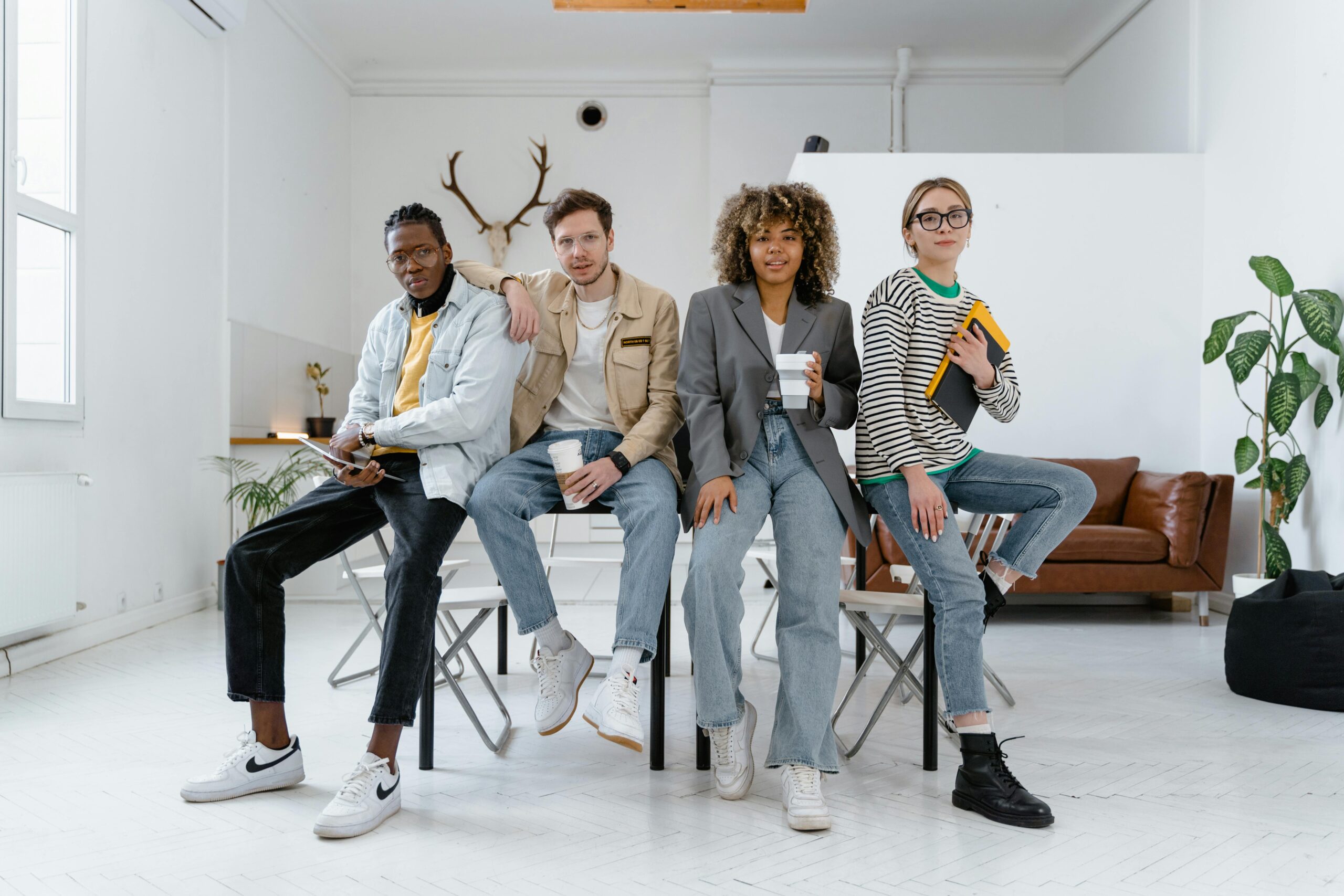 Group of four stylish young adults sitting casually in a modern studio.